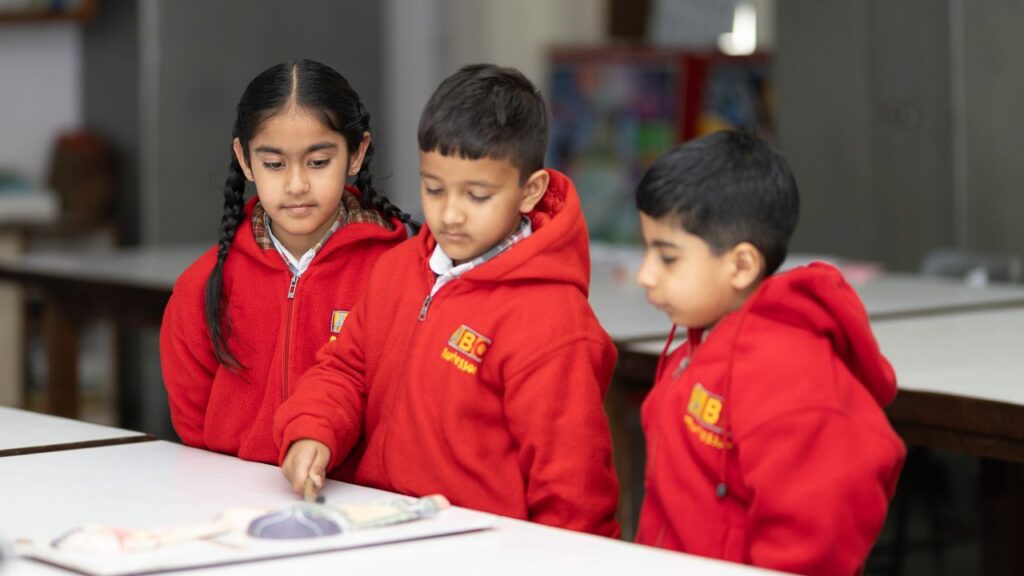 Three children wearing red uniforms engage in a classroom learning activity in Patiala, India.